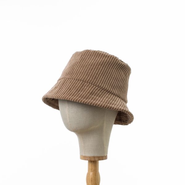 Side on view of Classic Bucket Hat made from thick ribbed beige corduroy fabric. The hat is in profile .The hat is positioned on a wooden hat stand.