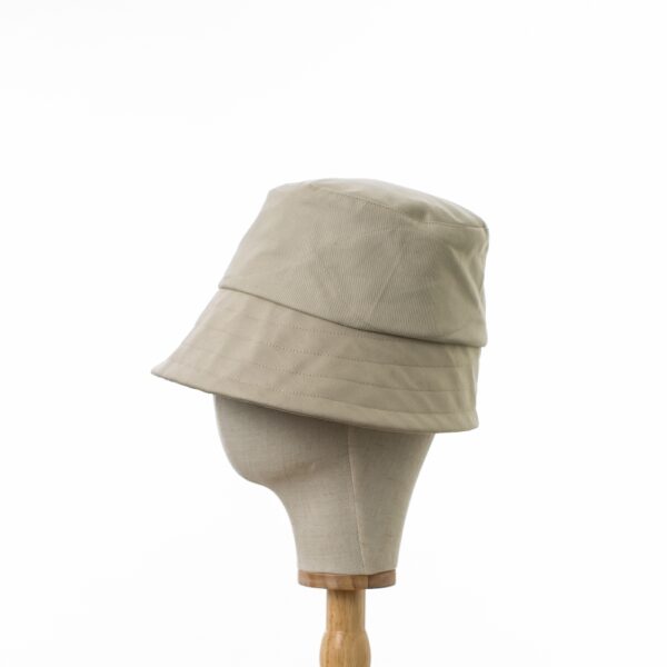 Chic Bayler and Co Bucket Hat made from 100% cotton beige drill fabric. Viewed in profile on a wooden and canvas hat stand