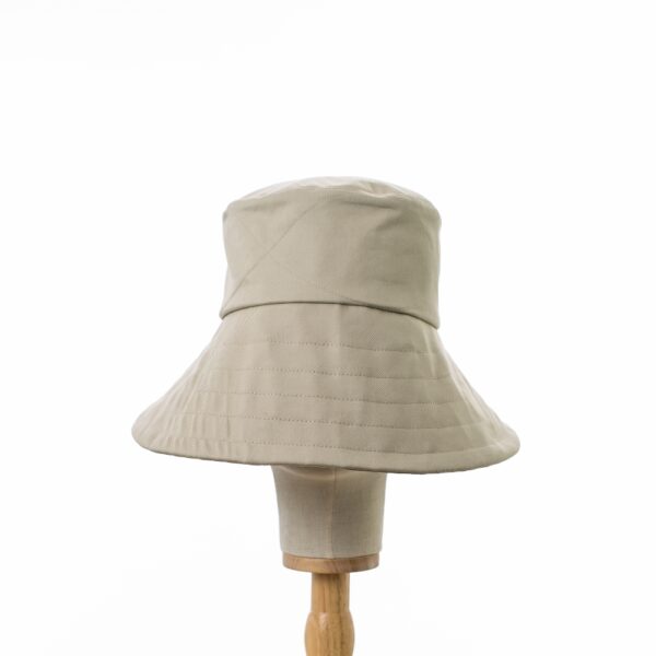 Elegant Bayler and Co wide brimmed Sun Hat made from 100% cotton beige drill fabric. Displayed on a canvas and wooden hat stand on a white background.