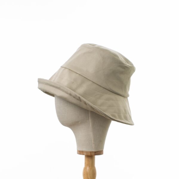 Elegant Bayler and Co wide brimmed Sun Hat made from 100% cotton beige drill fabric. Displayed on a canvas and wooden hat stand on a white background. Profile view. With upturned brim.