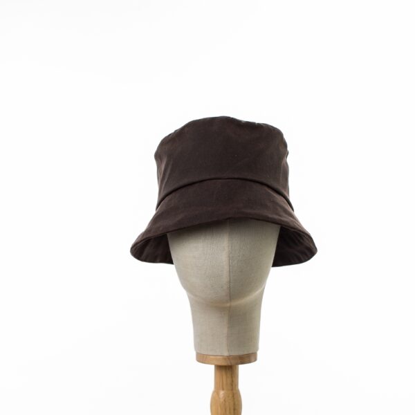 Chocolate Brown showerproof rain hat. Made from vintage look durable waxed cotton. displayed on a canvas and wooden hat stand on a white background.head on view.