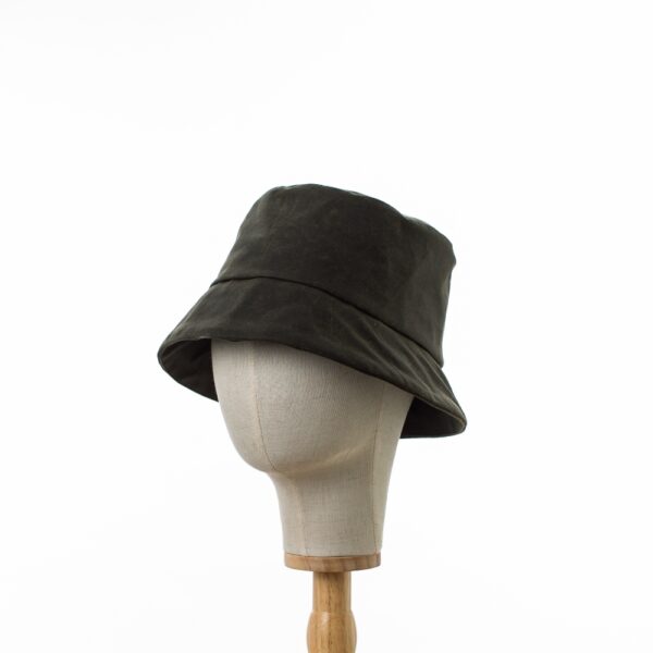 Chic and Practical Bayler and Co Dark Green shower proof rain hat. Made from vintage look durable waxed cotton. displayed on a canvas and wooden hat stand on a white background.slightly turned to the side.