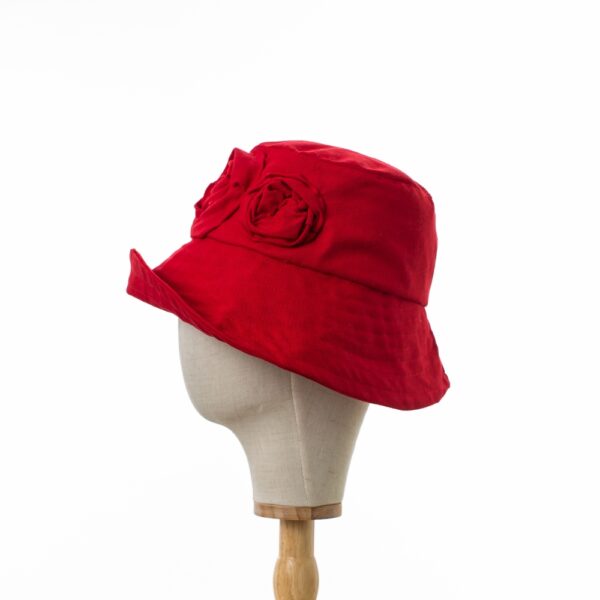 Elegant Bayler and Co wide brimmed Sun Hat with red roses made from 100% red cotton fabric. Viewed in profile with the brim upturned displayed on a canvas and wooden hat stand.
