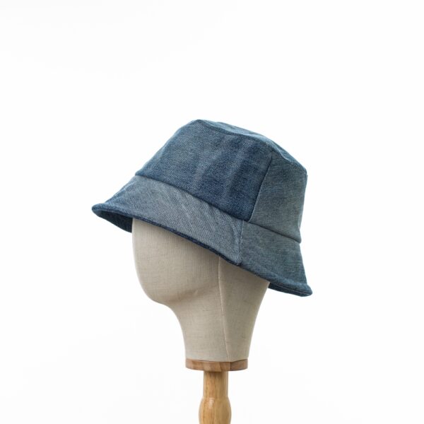 A side view of a Bayler and Co Upcycled Denim Bucket Hat. The hat is on a canvas hat stand and is seen in profile.